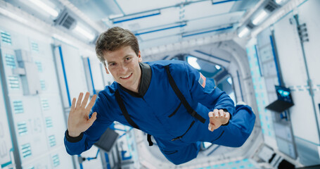 Portrait of Courageous Caucasian Male Astronaut on Board a Spacecraft, Floating in Zero Gravity and Smiling At The Camera, Waving. Space Travel, Solar System Exploration and Colonization Concept