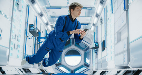 Male Astronaut Floating in Zero Gravity Inside a Space Station. Spaceman Using Smartphone in Space...