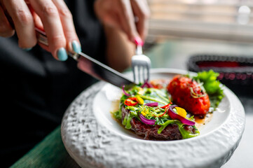 Close-up of hands using utensils to enjoy a gourmet dish garnished with edible flowers, embodying the concept of fine dining