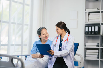 Fototapeta premium A woman in a white coat is sitting next to an older woman in a hospital bed