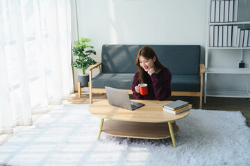 Asian woman is sitting on a coffee table with a laptop and a cup of coffee