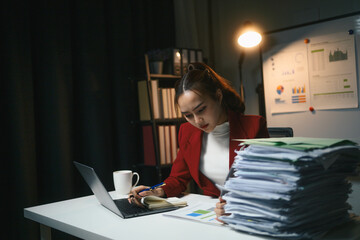 Business woman is sitting at a desk with a laptop and stacks of papers