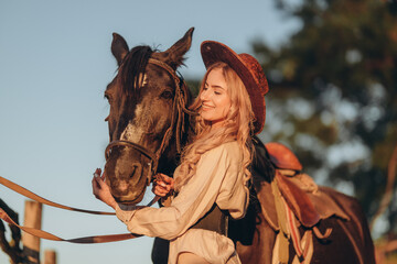 A young woman with a horse stands near a fence in autumn at sunset. Breeding thoroughbred horses...