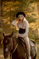 Fototapeta premium A young beautiful woman rides a horse in the forest in autumn. Horseback riding in the evening in autumn.