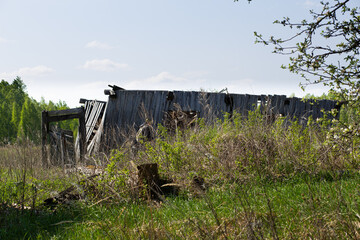 Ruins of a traditional village house. The old central residential architecture of Russia is destroyed and abandoned. Log cabin against a background of gray sky and green grass