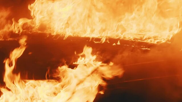 A vehicle is consumed by a voracious fire, leaving only the suggestion of its former shape amidst the fiery chaos.