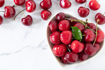 Fresh ripe cherries in a heart-shaped bowl on white kitchen table. Top view. Copy space. Sweet summer fruit.
