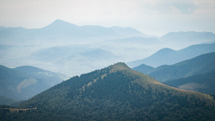 Obraz premium Hilly landscape with green mountain in the foreground and layers of mountains in backdrop, Europe