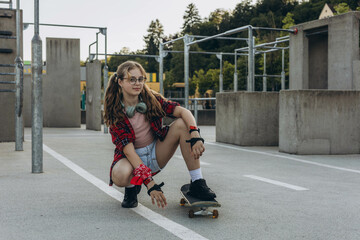 Teen girl skater with a skateboard is sitting and resting in the skaters park