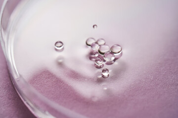 Serum or cosmetic oil flows into a transparent bowl on a purple background.