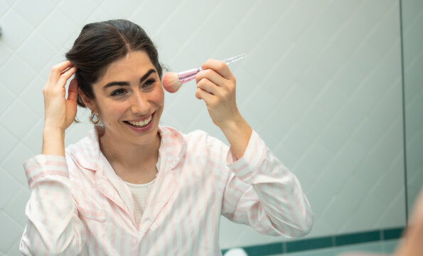 Young woman applying fard while looking in the mirror in bathroom