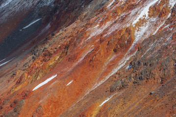 Natural texture of multicolor rocky mountain wall in sunlight. Minimal nature backdrop of multi-colored vertical rocks close up. Freshly fallen snow on colorful rockies. Minimalist vivid background.