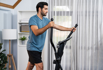 Athletic and sporty man running on elliptical running machine during home body workout exercise...