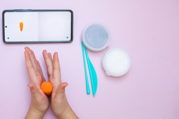 The child sculpts a figure from plasticine and looks at the phone.