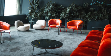 Orange lounge chairs and sofa on a gray carpet with a dark background with monstera plants. I small round coffee table completes this modern and minimalistic interior design..