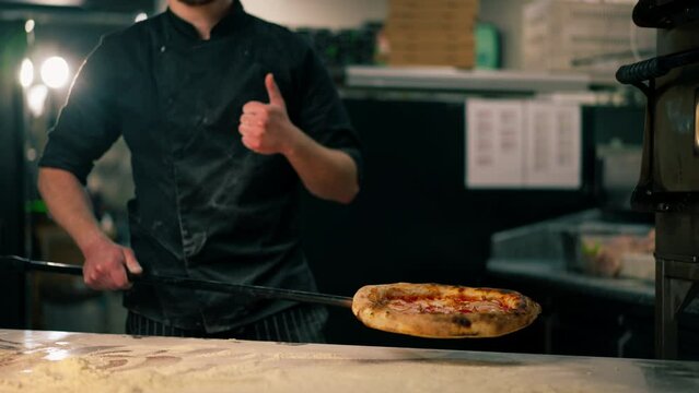 in a professional kitchen in a pizzeria the chef holds freshly prepared pizza on a shovel