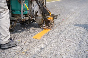 Man use thermoplastic road marking paint machine, hot melt marking paint machinery spraying a yellow line on concrete road.