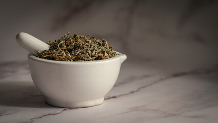 Close-up of Dry Organic Marijuana (Cannabis sativa) leaves, in white ceramic mortar and pestle, on a marble background.