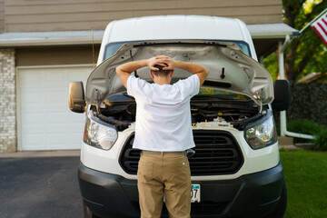 Stressed man having trouble with his broken car looking in frustration at failed engine