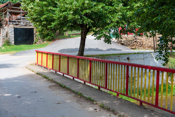 Rural Charm. Colorful Bridge Fence with Yellow and Red Paint, Black Garage Door Framed by Trees