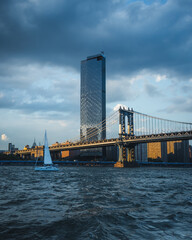 New York waterfront with a sailboat and a bridge. In the background a Skyscraper located in Manhatten...