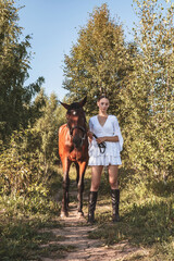 Fototapeta premium A young girl in a white dress stands next to a horse.