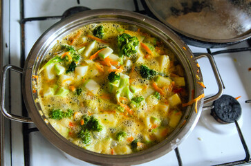 A boiling pot of colourful vegetable soup steaming on top of the stove.