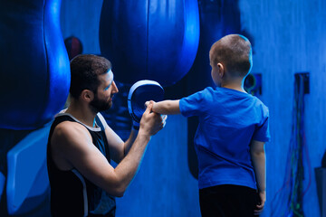 Coach helps a child put on boxing gloves. Young boy boxer with trainer in gym