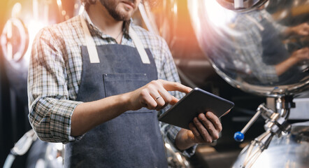 Worker man in apron use digital computer tablet for control quality of beer drink tank. Banner technology on brewery factory, sunlight
