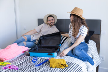 happy young couple packing things into suitcase for summer vacation