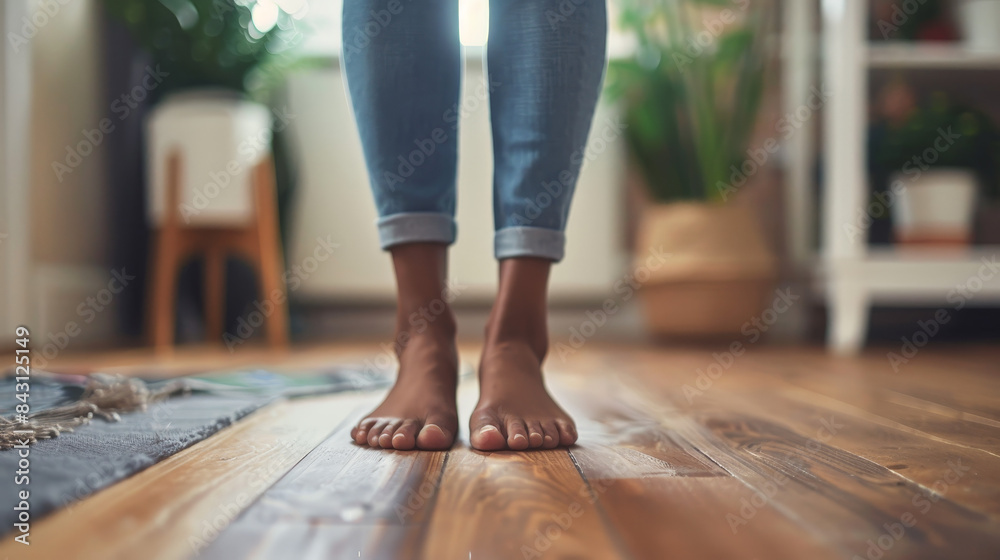 Wall mural a black woman stands on a wooden floor indoors, her feet clad in shoes, with furniture and clothing 