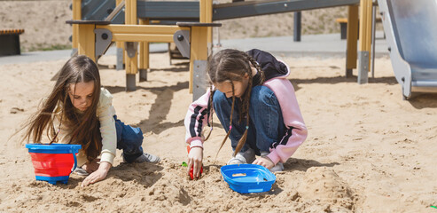 Little children playing with toys in sand box outdoors