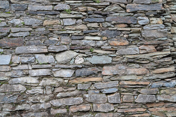 Ancient wall made of slim natural rocks with green plants and moss growing between stones as an architectural background