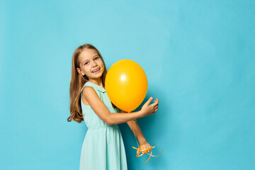 Joyful little girl in a dress holding a bright yellow balloon against a vibrant blue background