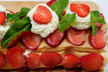 Close-up of part of a freshly made tiramisu cake with strawberries and mint leaves.