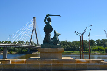 Warsaw, Poland. Statue of Mermaid (Polish: Warszawska Syrenka) symbol of Warsaw by the Vistula river on the background of Swietokrzyski Bridge. Spring time in Warsaw, Poland © PaulSat