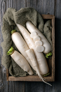 Ripe white daikon radish roots in wooden box on rustic wooden table close up. Food photography