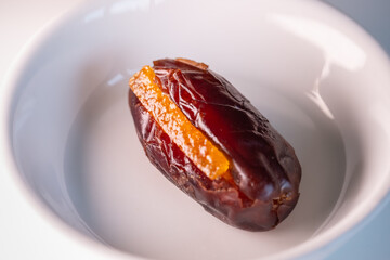 closeup top view of a white porcelain plate with a magnificent large fresh Dubai date filled with pieces of candied orange pieces