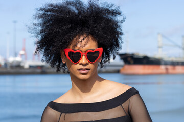 Non-binary person with afro hair and heart-shaped sunglasses, looking straight ahead