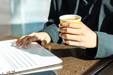 Person wearing a black suit holding a yellow coffee mug while working with their laptop