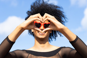 Concept of love: Non-binary person with heart-shaped red glasses and afro hair, making a heart shape with their hands