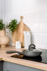 Selective focus on frying pan with lid on modern induction stove at kitchen