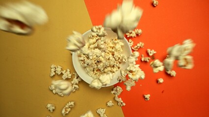 Top down view of flying popcorn dropping at white bowl with yellow and orange background. Super...