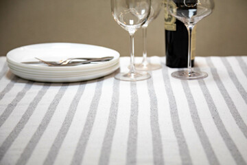 Table set neatly on a white striped tablecloth, bottle of wine, crystal glasses, white plates and cutlery