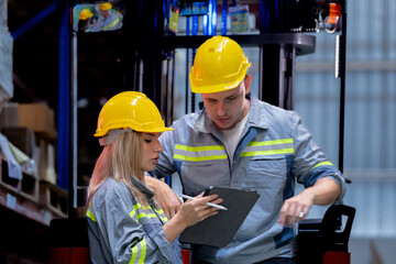 Two male and female factory checkers are discussing work on a warehouse truck. While working in a warehouse for industrial products