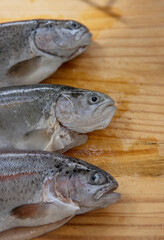 Carving three raw fresh trouts on the old wooden cutting board. Cooking whole freshwater rainbow forel. Oncorhynchus mykiss on the chopping plate. Wood background. Close up. Copy space. Top view