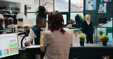 African american guy picking up order from clothing store, signing confirmation papers at cash...