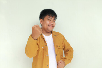 Happy excited and smiling young Asian man raising his arm up and and scream to celebrate success or achievement. Isolated in gray background.