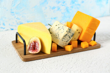 Wooden board with tasty cheese on table near blue wall