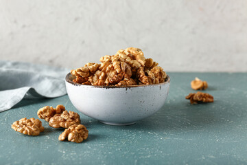 Bowl of tasty walnuts on table against white wall